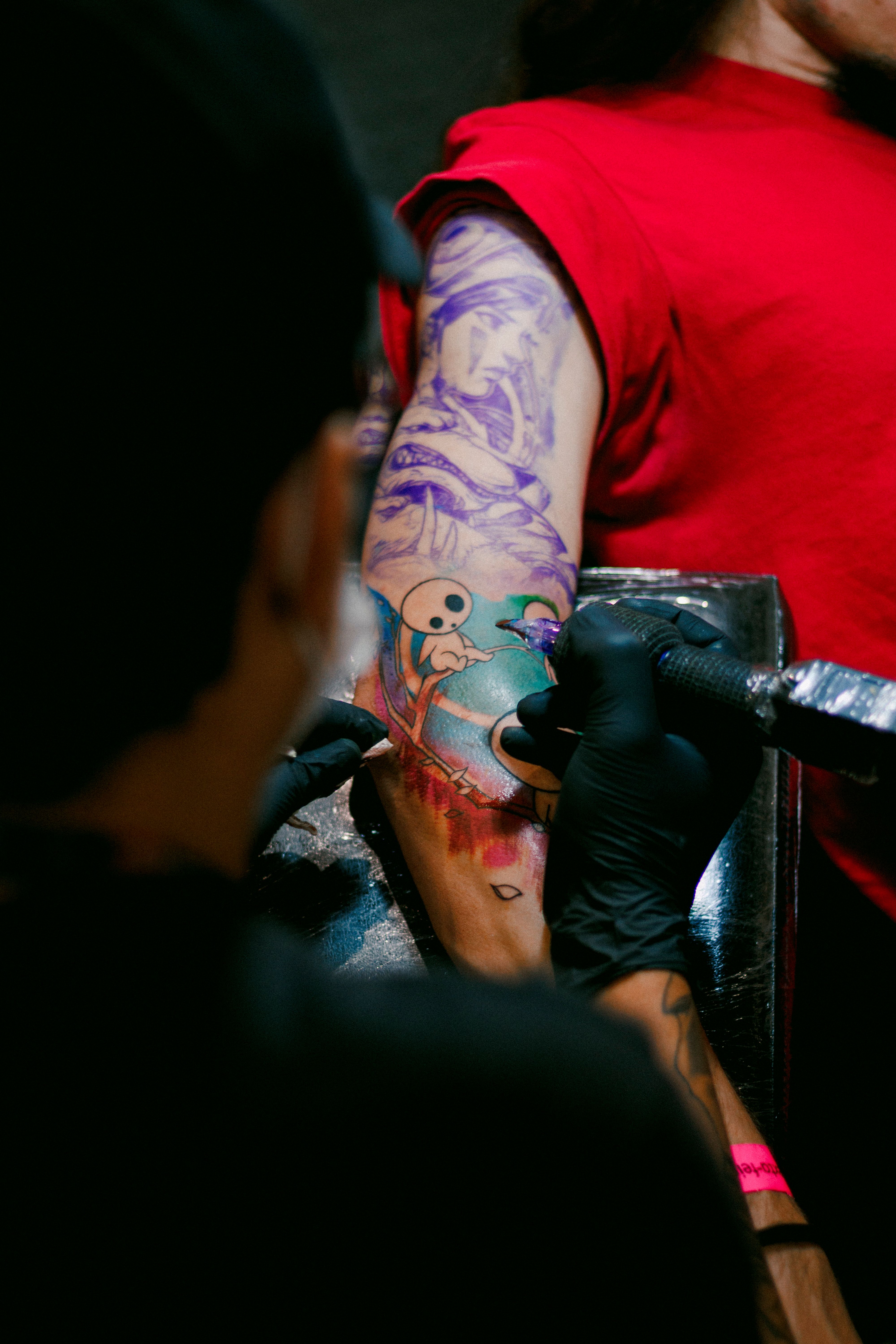 Artist tattooing colorful design on arm in studio setting.