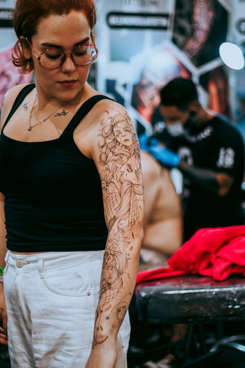 Free Woman showcasing a floral sleeve tattoo in a contemporary tattoo studio setting. Stock Photo