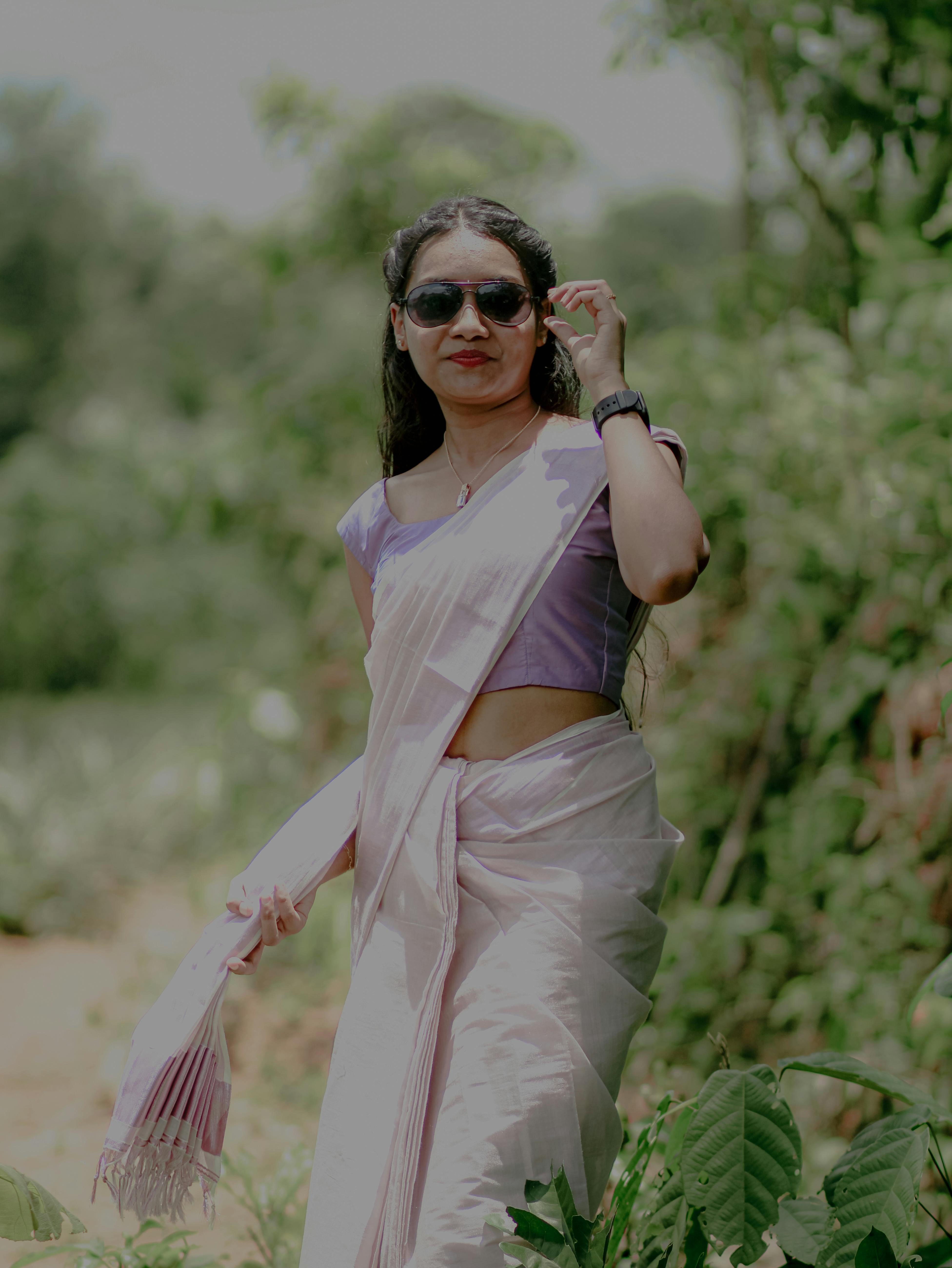 South Asian woman in a white saree and sunglasses enjoying an outdoor setting.