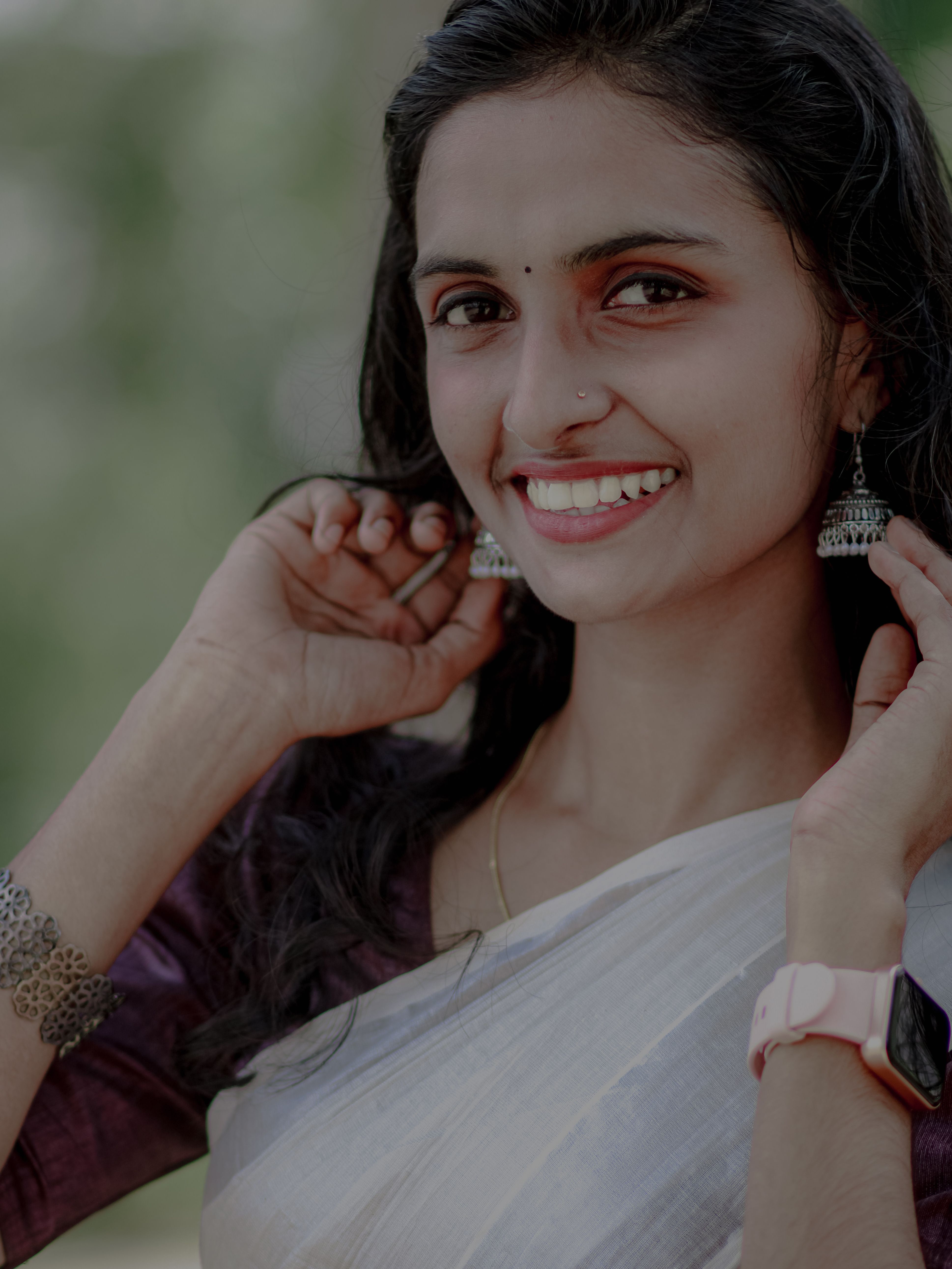 A smiling woman wearing traditional Indian attire and jewelry outdoors, exuding charm and elegance.