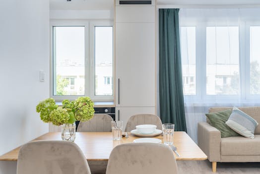 Bright modern dining area with wooden table, hydrangeas, and large windows providing natural light.