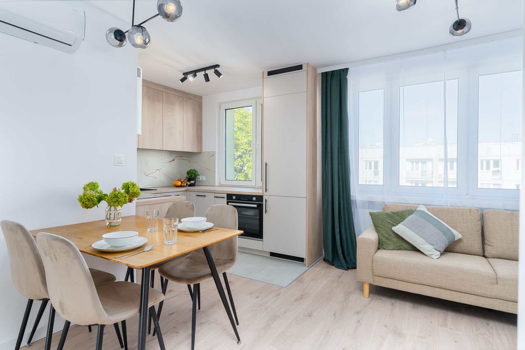 Pale kitchen beside a wood dining table, upholstered chairs, green curtain and sofa