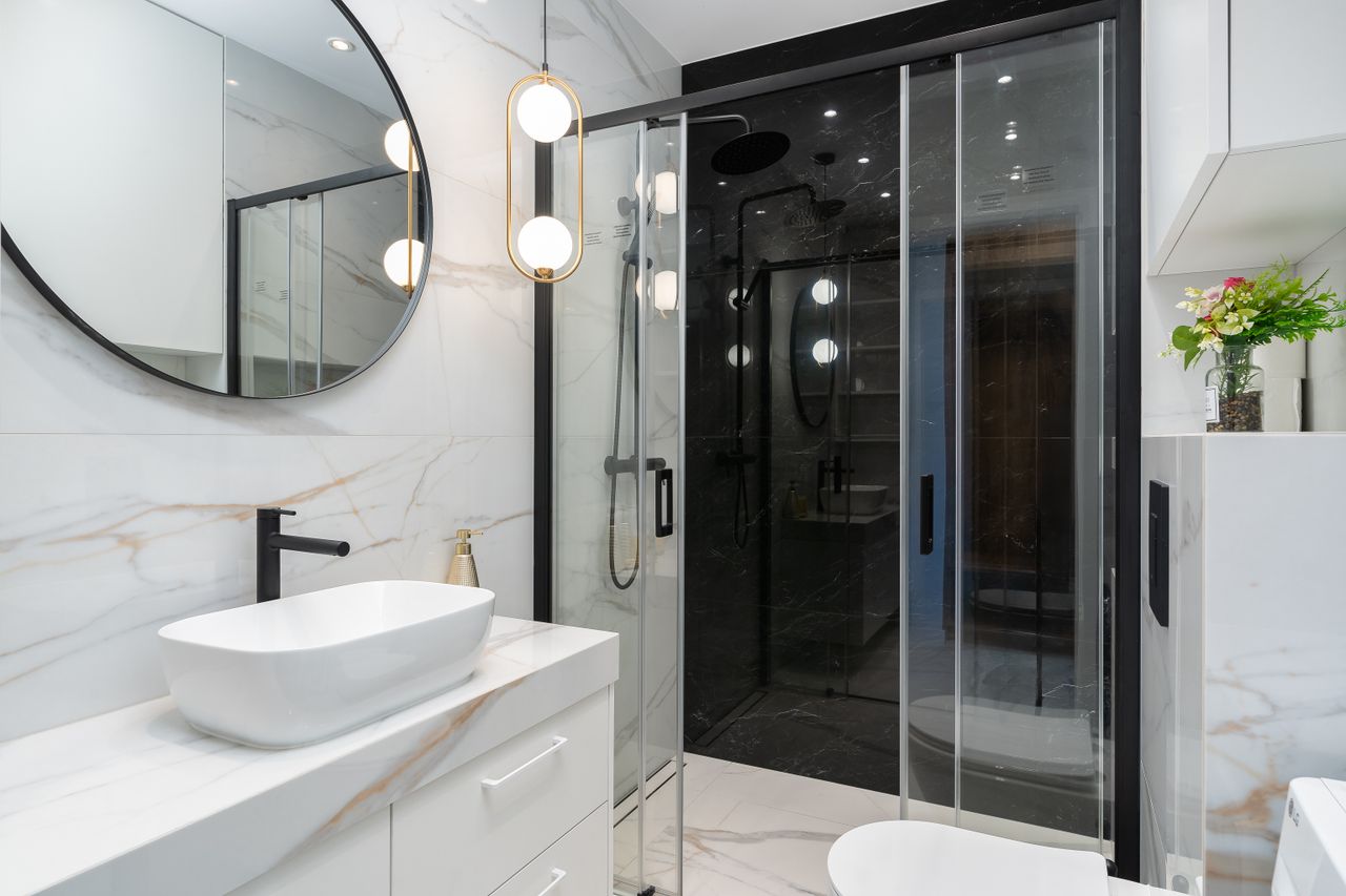 Gold globe pendant light hanging beside a glass shower enclosure in a modern marble bathroom