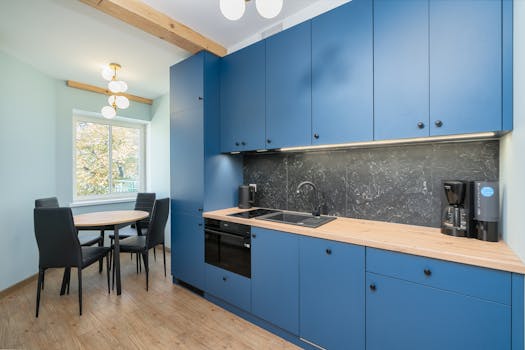 Stylish kitchen featuring blue cabinets and a minimalist dining area with natural light.