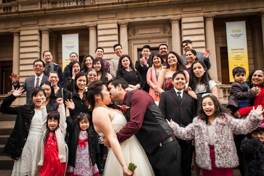 A happy wedding couple kissing with a jubilant crowd outside a historic building in Melbourne.