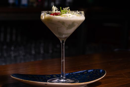 A stylish cocktail glass filled with a creamy dessert topped with garnish on a rustic table.