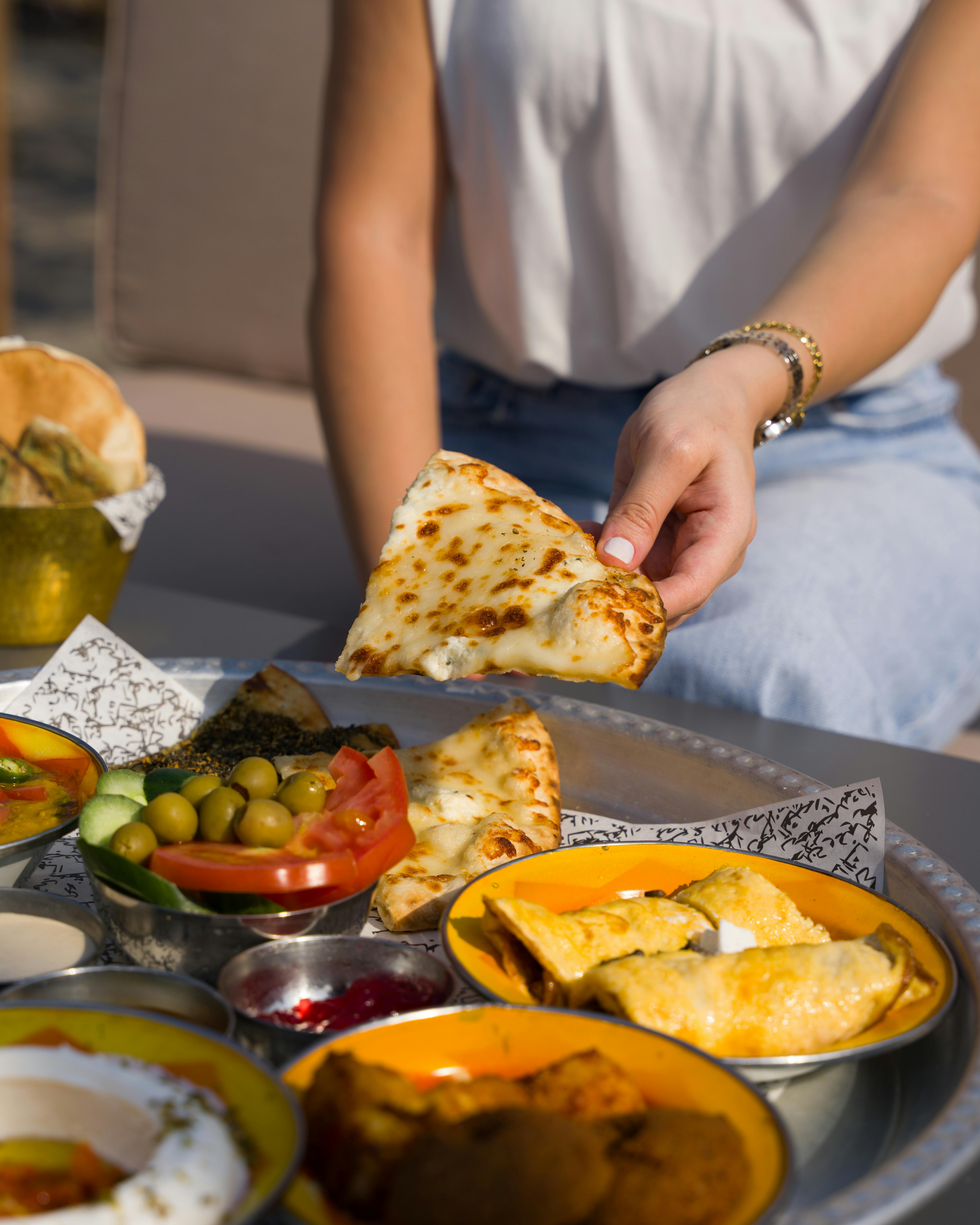 A selection of Middle Eastern dishes on a table with a person enjoying fresh bread.