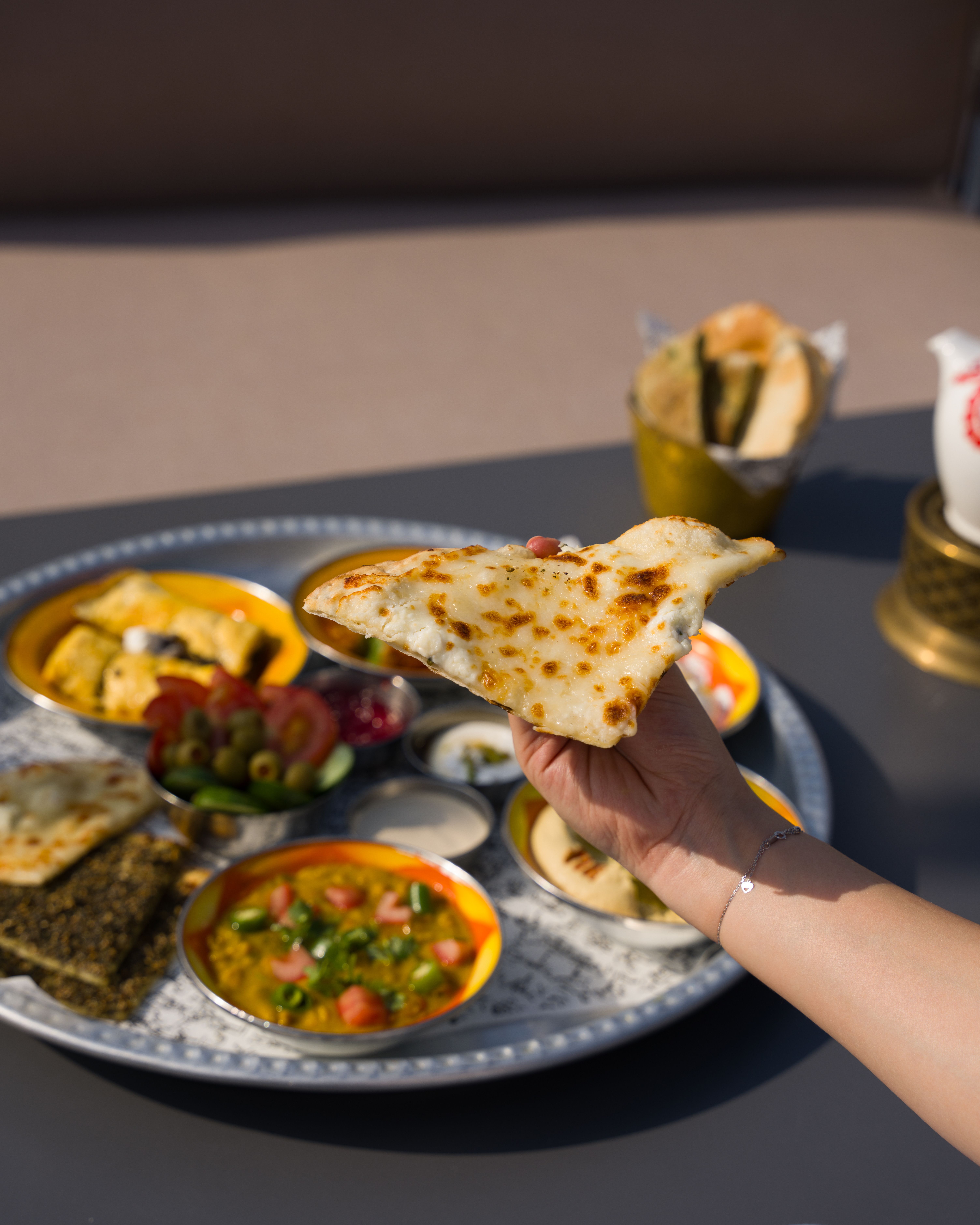 Hand holding naan with Indian thali, vibrant vegetarian dishes.
