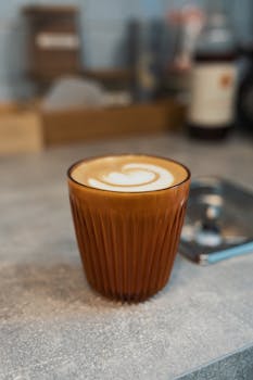 Brown glass with latte art on a cafe counter, subtle and warm ambiance.