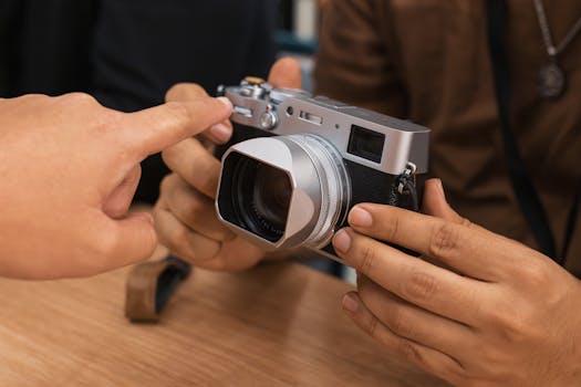 Close-up of hand pointing to a digital camera held by another person indoors.