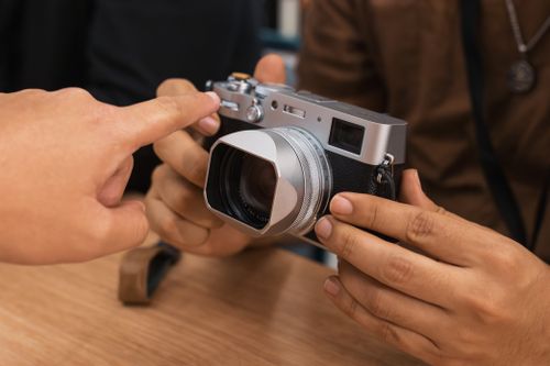 Free Close-up of hand pointing to a digital camera held by another person indoors. Stock Photo