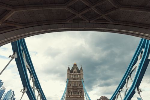 Free View of the Tower Bridge tower framed by the bridge's arches against a cloudy sky. Stock Photo