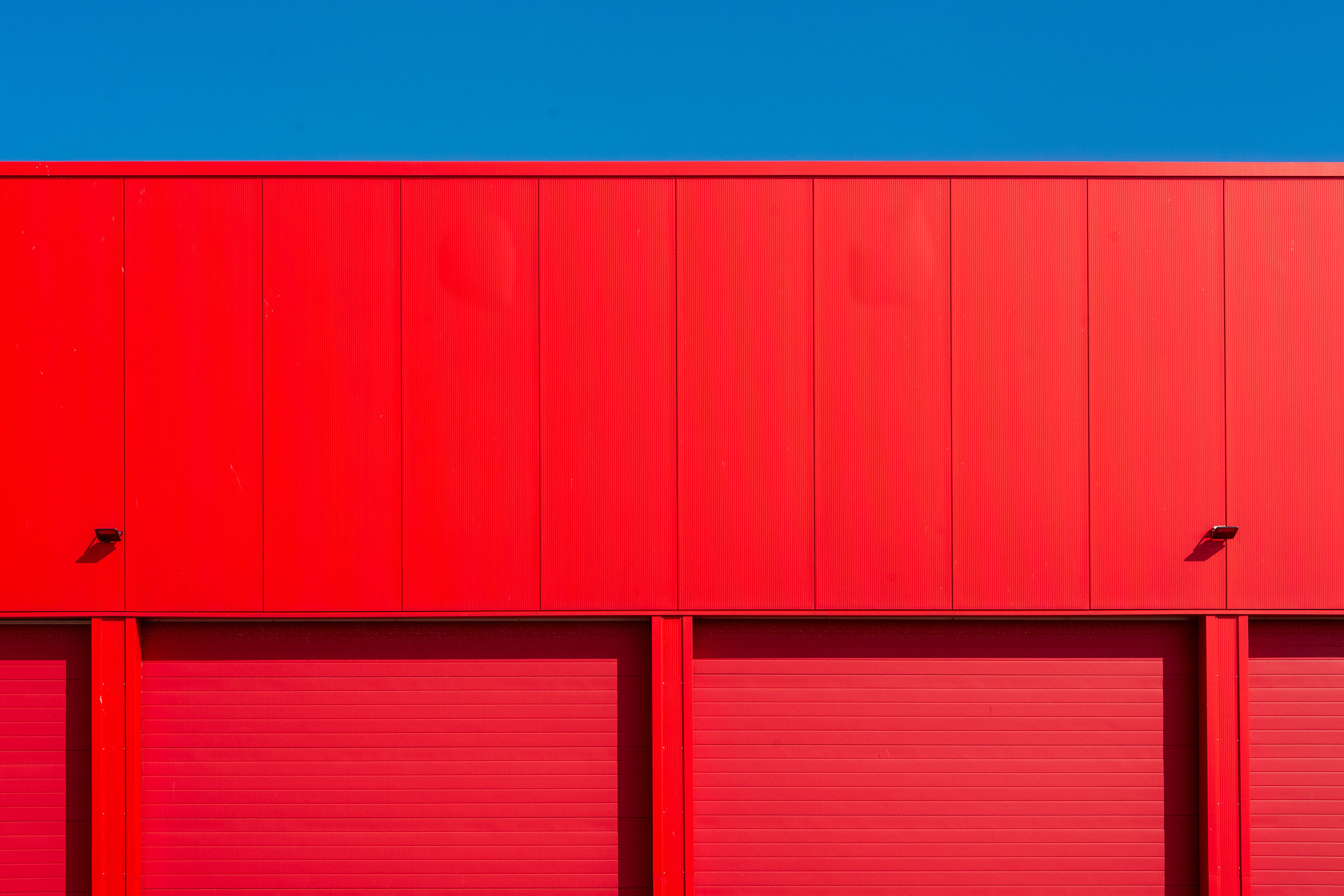 Bright red garage doors of an industrial building against a clear blue sky, showcasing minimalism.