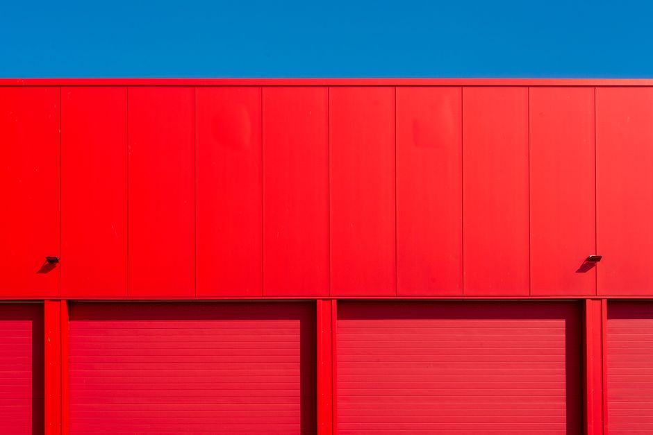 Bright red garage doors of an industrial building against a clear blue sky, showcasing minimalism.