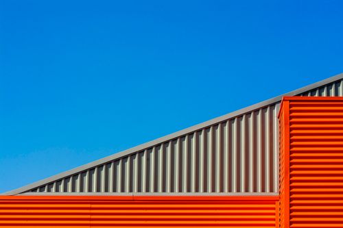 Free Vibrant architectural shot of a modern industrial building with orange and gray elements set against a clear blue sky. Stock Photo