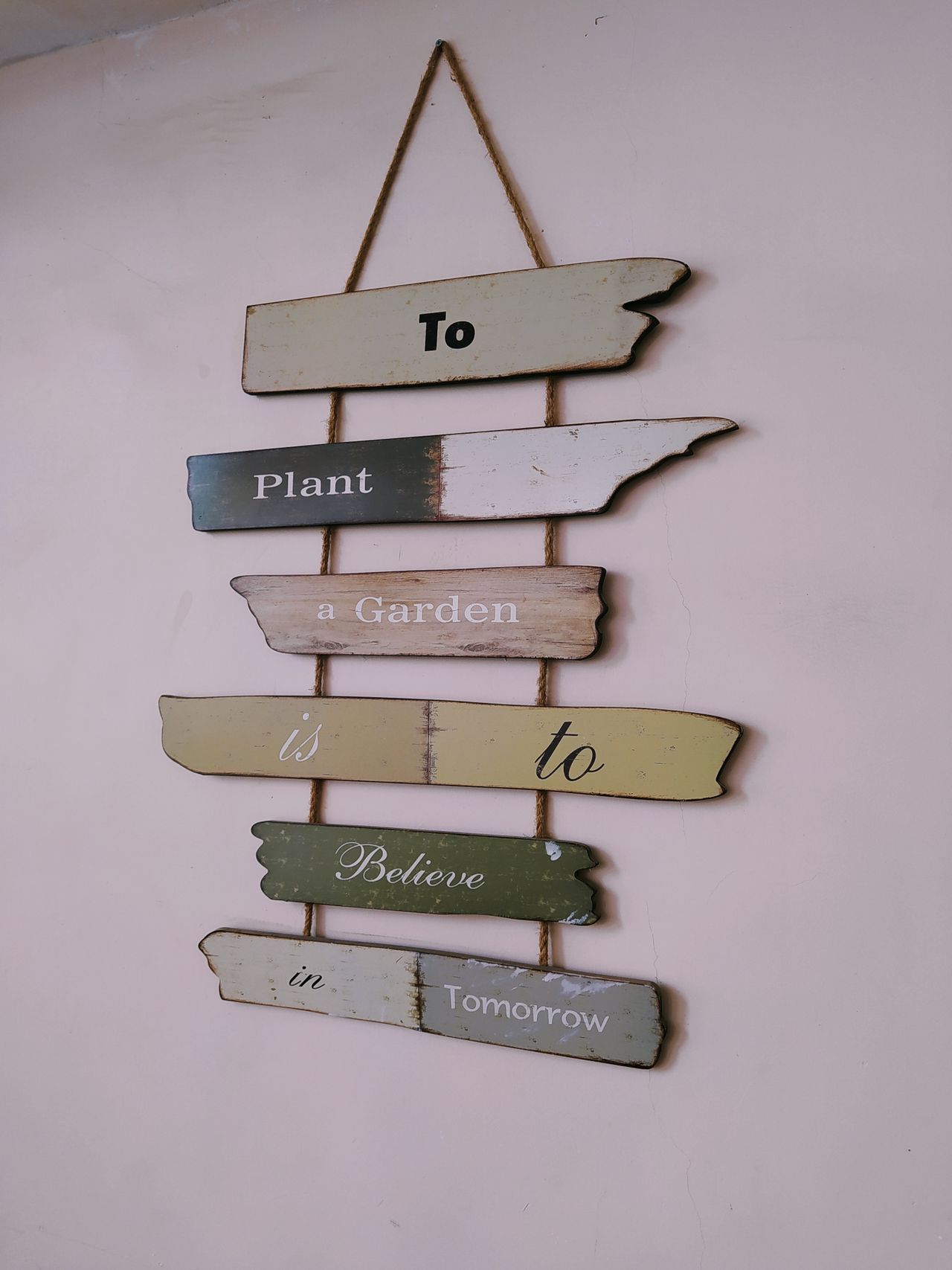 A hanging wooden plank sign painted with a garden quote in soft, weathered colors