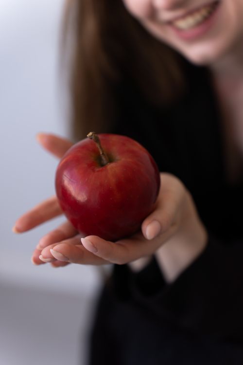 Free A smiling woman presents a vibrant red apple in her hand, symbolizing health. Stock Photo