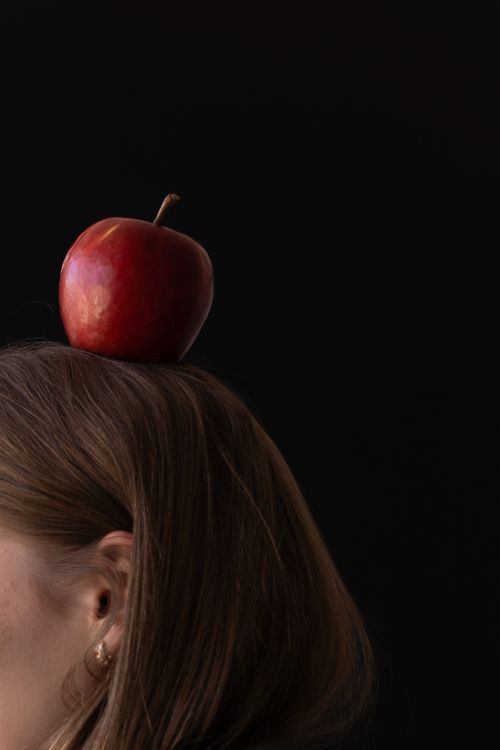 Free Creative portrait of a person with an apple balanced on their head against a dark background. Stock Photo