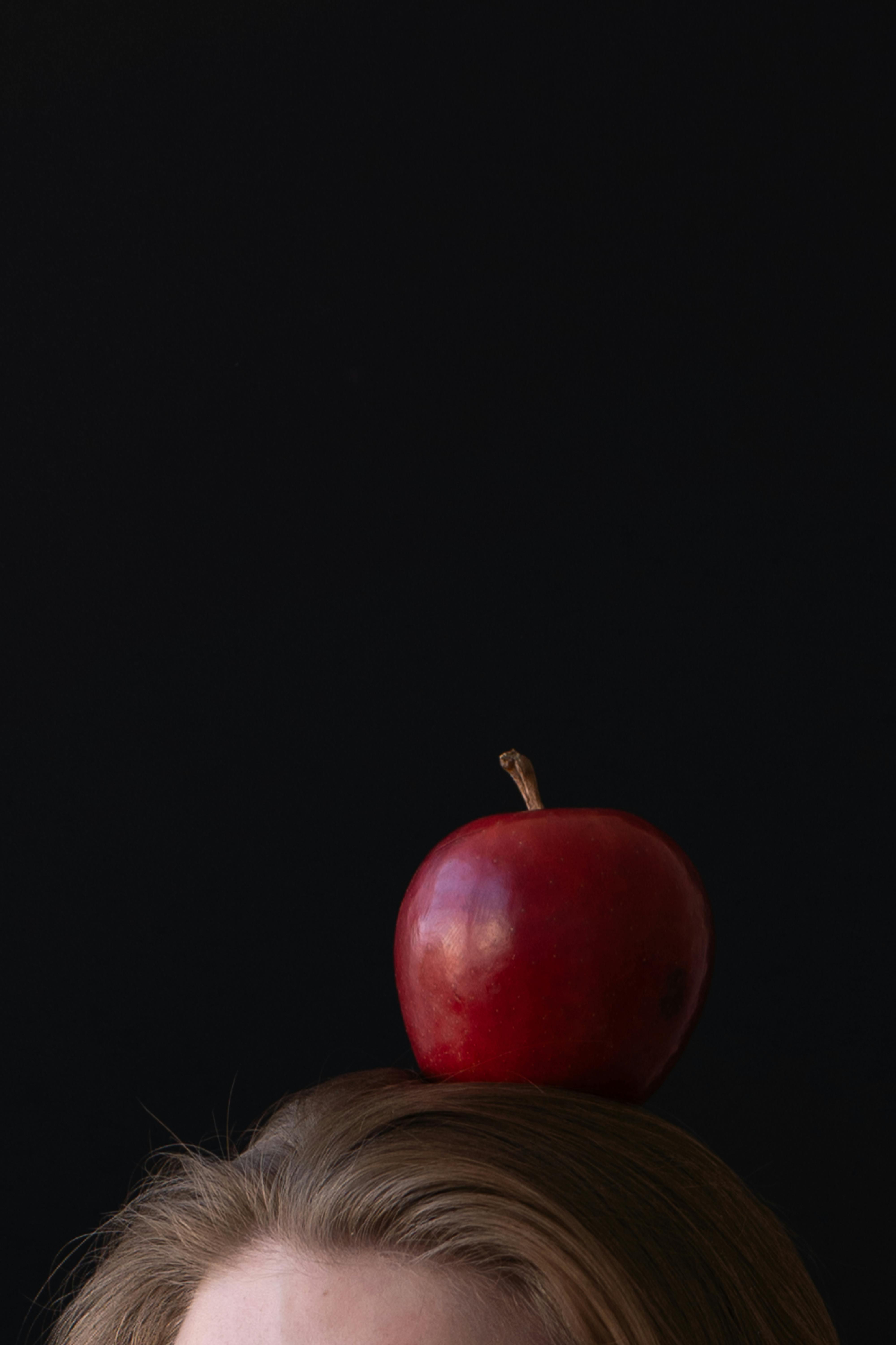 무료 어두운 배경에 사람 머리 위에 있는 붉은 사과의 클로즈업. 균형을 상징합니다. 스톡 사진