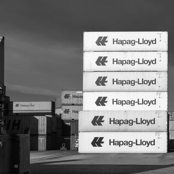 Stacked Hapag-Lloyd shipping containers at the Hamburg port in a monochrome setting.