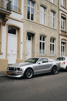 A silver Mustang parked on a charming urban street with classic architecture.