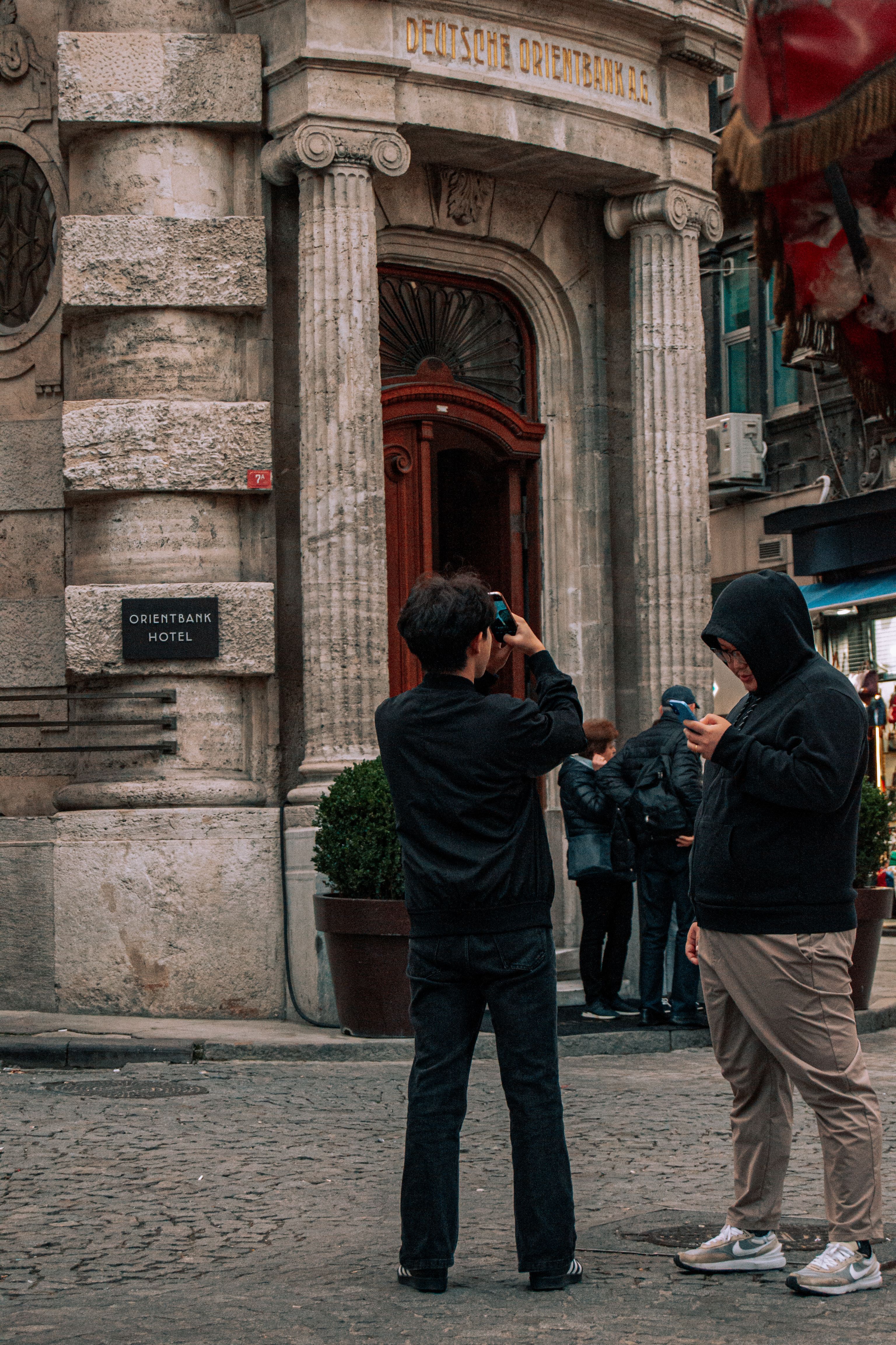 Two tourists capturing the iconic Orientbank Hotel facade on a city street.
