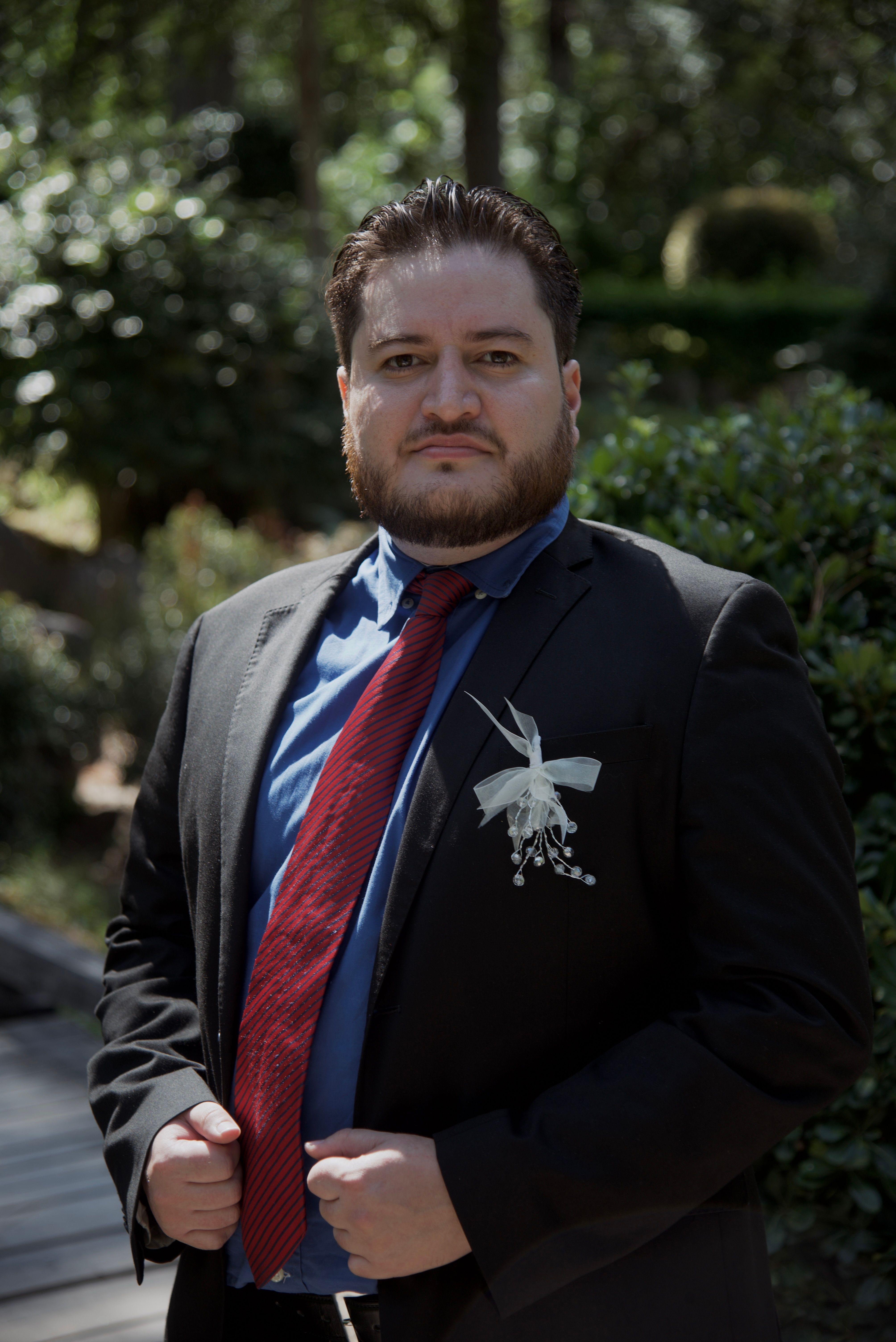An outdoor portrait of a man in formal attire with natural greenery background.