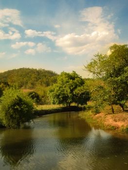 Peaceful river scene with lush greenery and hills under a bright sky. - Fotografer Sidoarjo
