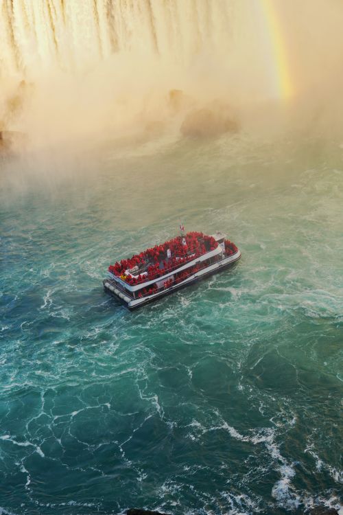 Free Experience the majestic view of Niagara Falls with a vibrant boat tour under a beautiful rainbow. Stock Photo