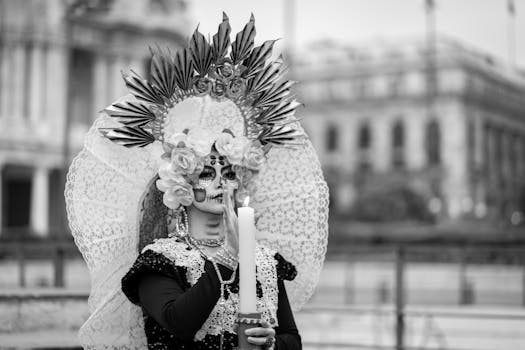 A person in elaborate Catrina makeup and costume holding a candle, celebrating Mexican tradition.