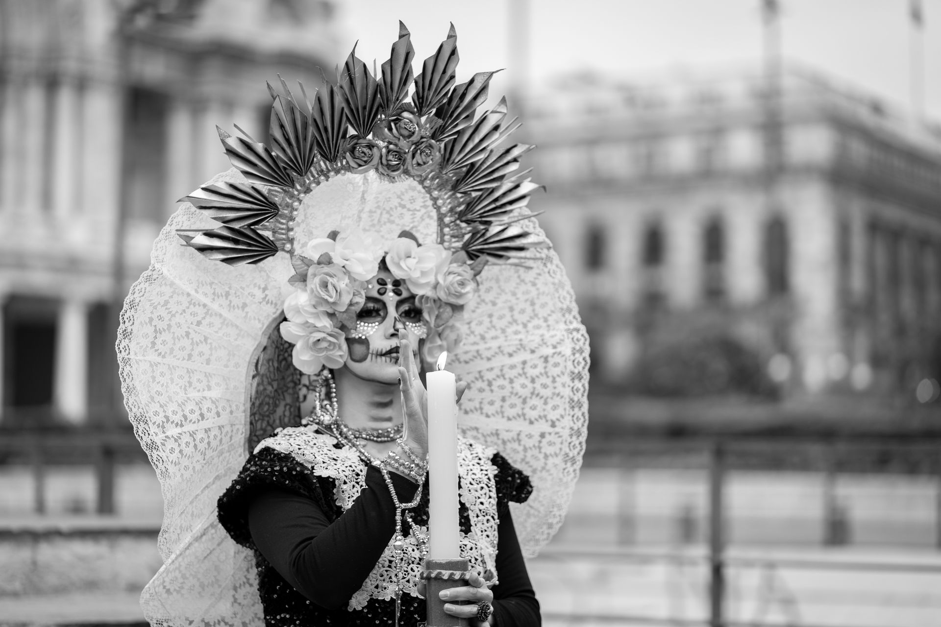 A person in elaborate Catrina makeup and costume holding a candle, celebrating Mexican tradition.