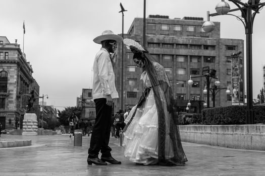 A couple in Catrina costumes on a bustling Mexican street.