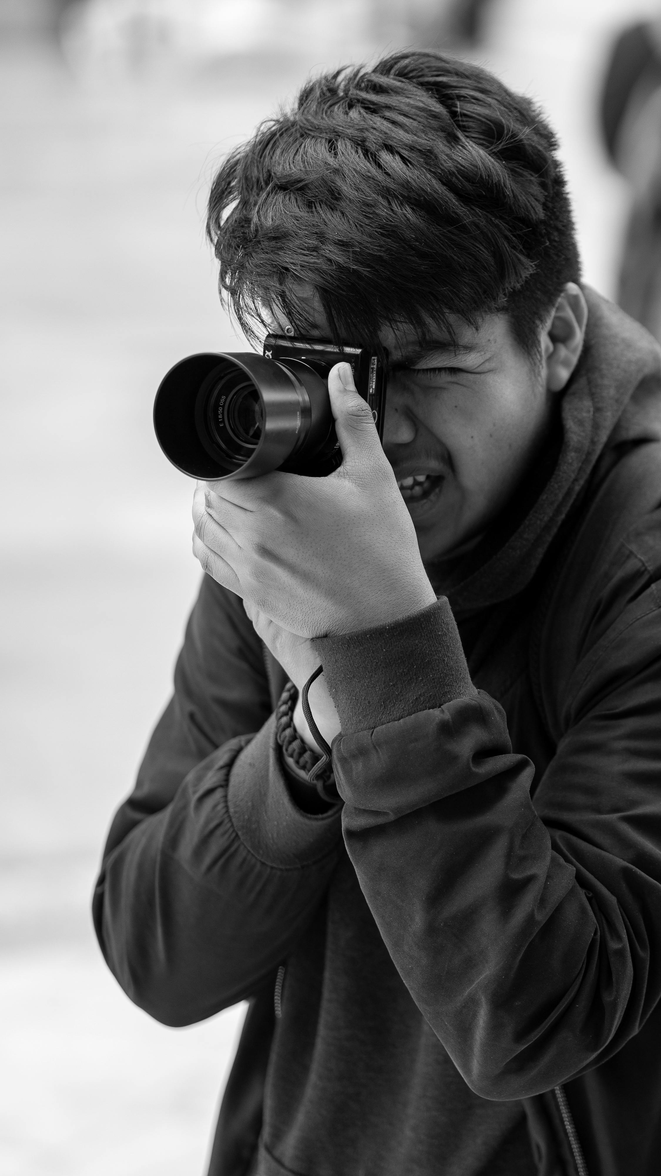 Monochrome image of young photographer focusing through camera outdoors.