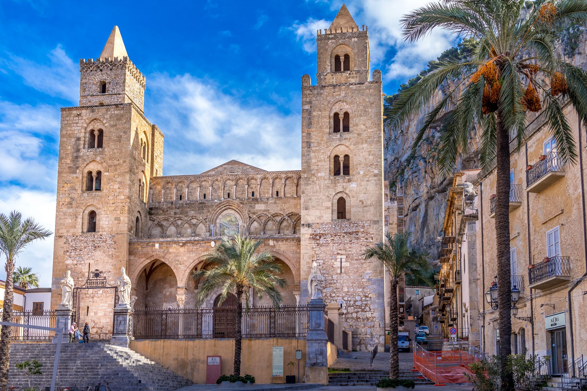 Cefalù Norman cathedral twin towers rising above old-town rooftops with the Tyrrhenian coast below