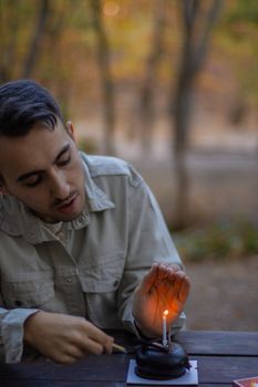 Young man lighting a candle on a small cake in a serene outdoor forest setting.
