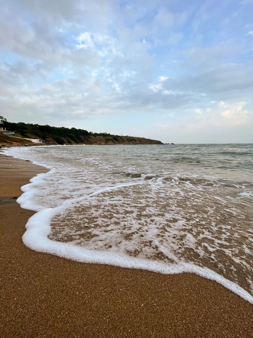 Free Peaceful beach with gentle waves lapping at the shore under a cloudy sky. Stock Photo