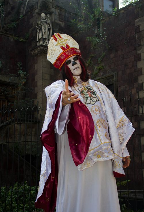 Free A person dressed in a priest costume with ornate skull face paint, set against a gothic backdrop. Stock Photo