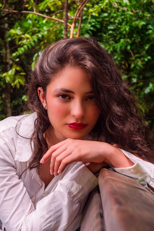 Free Captivating portrait of a young woman in a white shirt against a vibrant green forest backdrop. Stock Photo