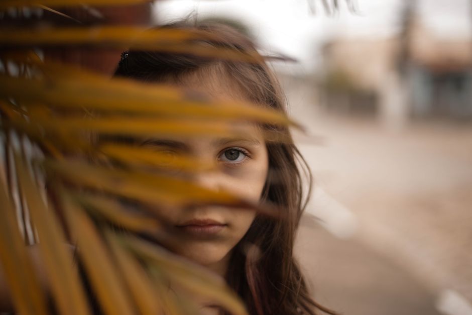 Niña joven parcialmente oculta por hojas en un entorno al aire libre.