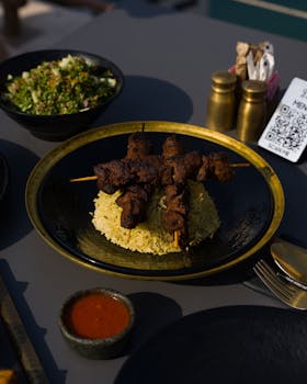 Savory grilled skewers served on spiced rice, accompanied by a fresh salad and sauce.