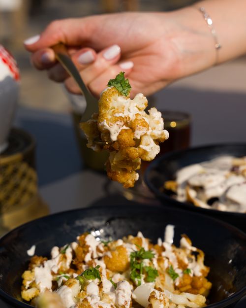 Free Close-up of crispy cauliflower bites topped with a creamy sauce, captured outdoors. Stock Photo