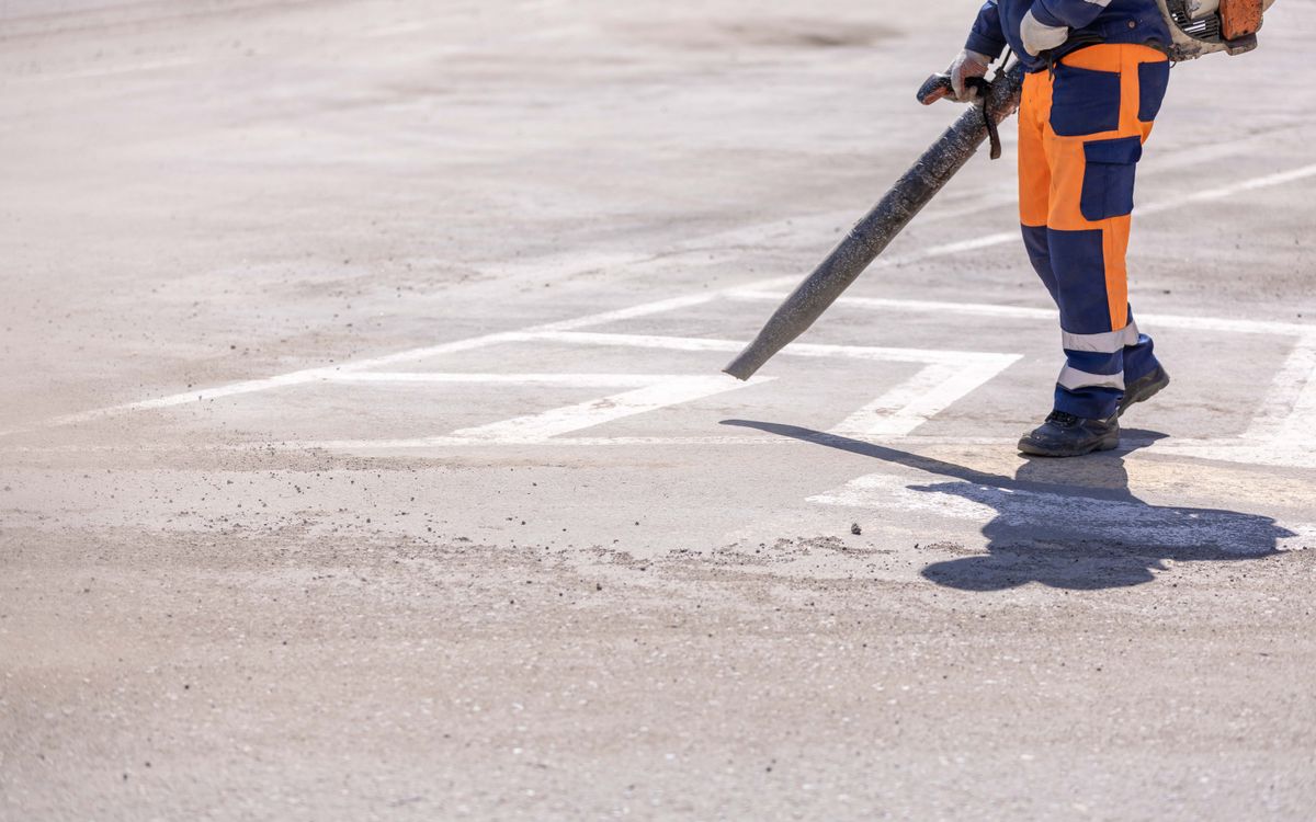 Construction worker clearing a site with an industrial blower on a sunny day.