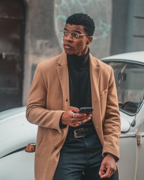 Free Fashionable adult man with glasses and coat using a mobile phone outdoors. Stock Photo