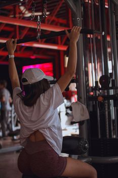 A young woman performs lat pulldowns in a gym setting, focusing on strength training.