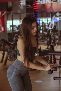 Young woman exercises with cable machine in a modern gym setting.