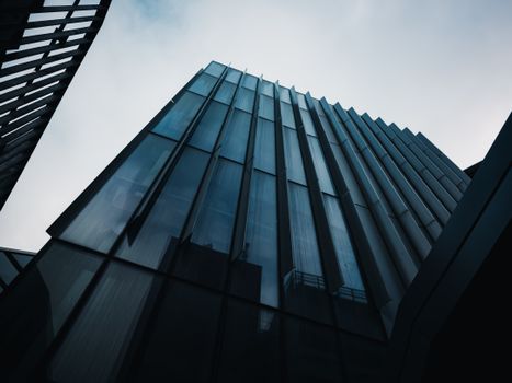 Low angle view of a modern glass skyscraper under a cloudy sky.