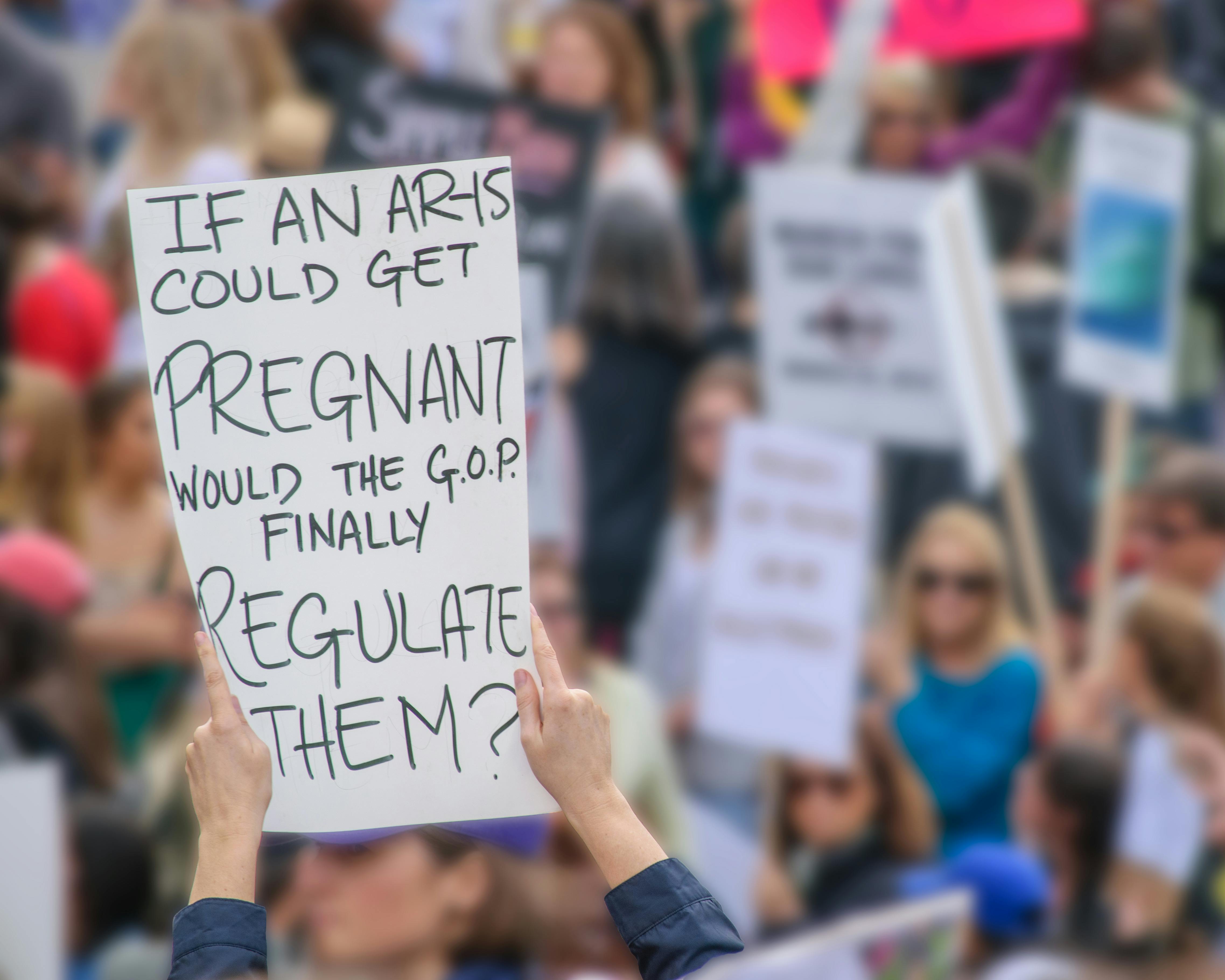 Crowd holding signs advocating for reproductive rights and regulation.