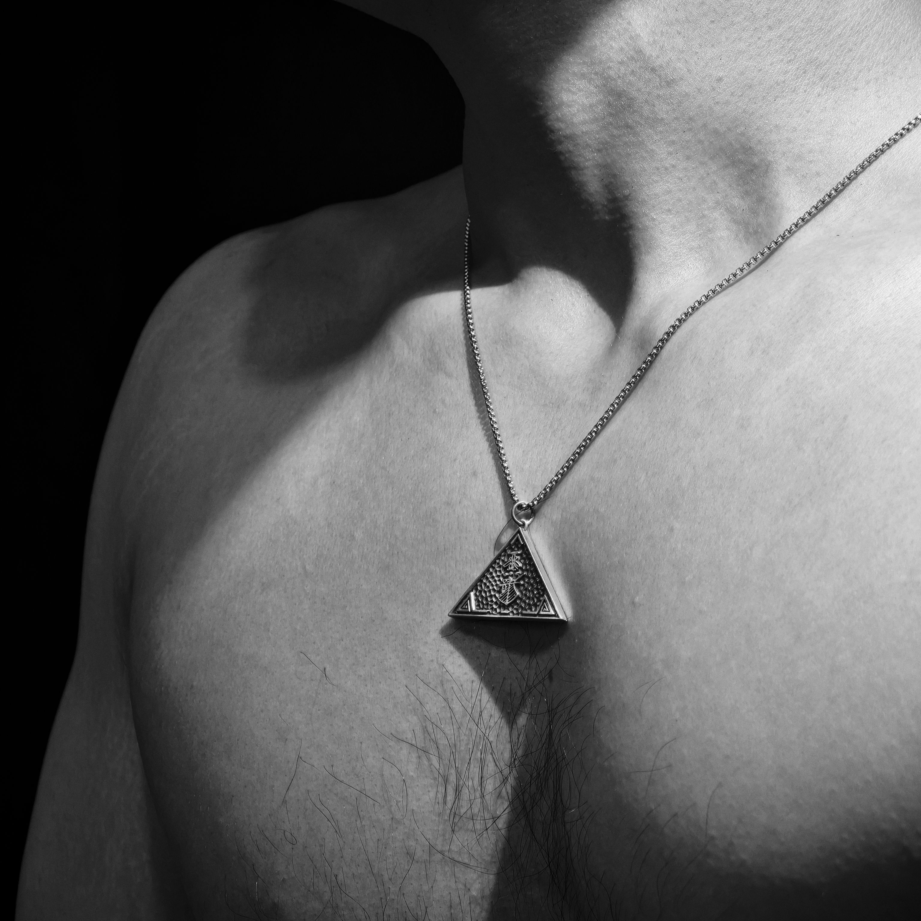Elegant black and white portrait showcasing a man wearing a triangle pendant necklace.