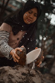 一名包着头巾的妇女在户外从椰子里倒出水，水花四溅