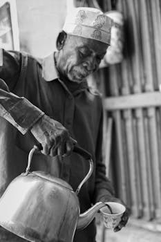 Black and white photo of an elderly man pouring coffee in Stone Town, Zanzibar. Captures traditional culture and serene lifestyle.